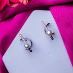 A pair of silver-colored pearl earcuffs displayed on a pink fabric.