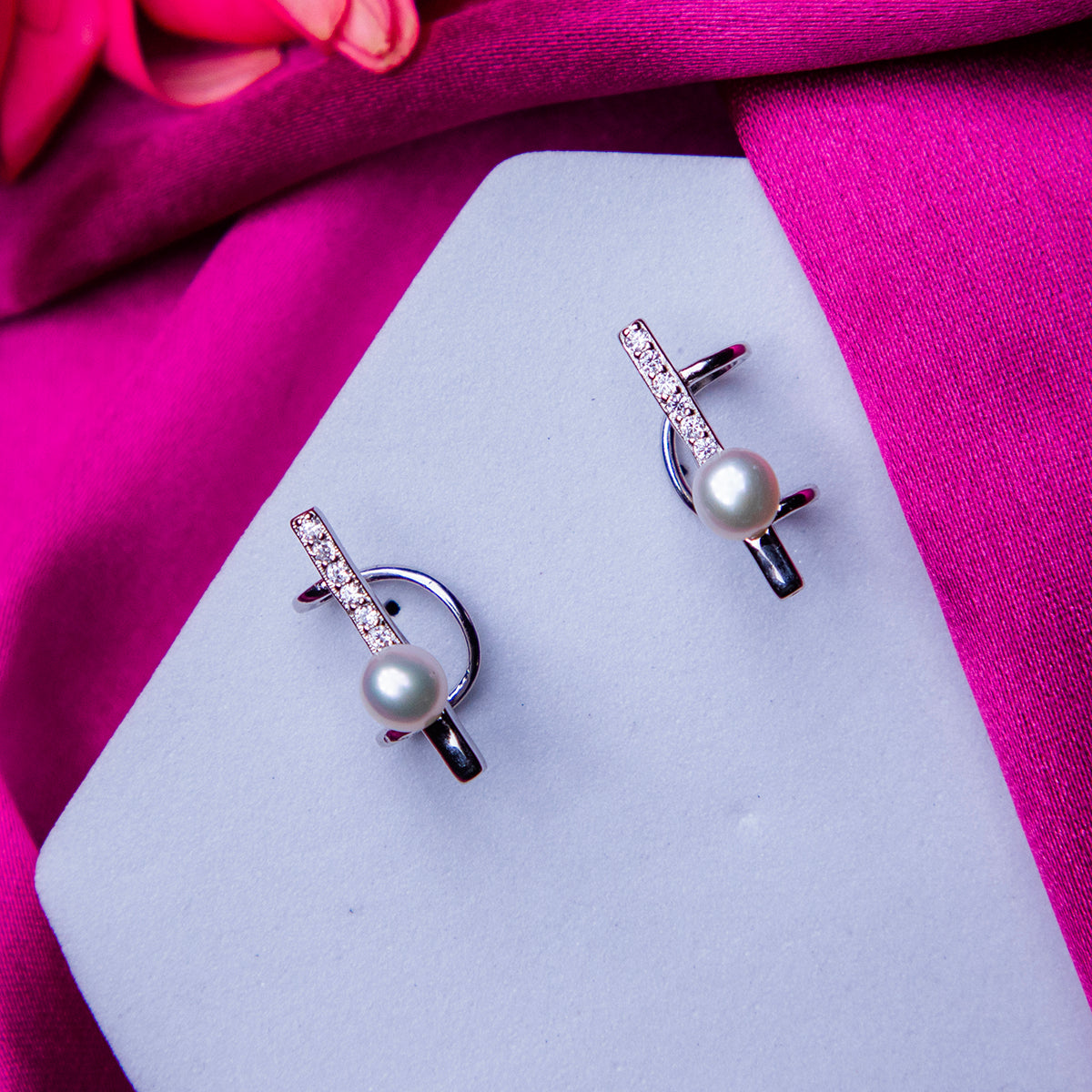 A pair of silver-colored pearl earcuffs displayed on a pink fabric.