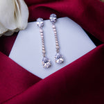 A pair of sterling silver drop earrings with white stones, displayed on a white stand with a red fabric backdrop.
