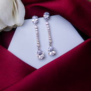 A pair of sterling silver drop earrings with white stones, displayed on a white stand with a red fabric backdrop.