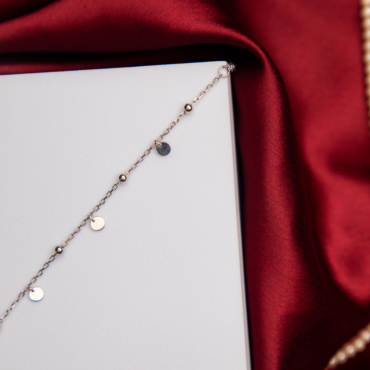 A Fine Silver Charm Bracelet with rhodium-based anti-tarnish coating, displayed on a red satin surface.
