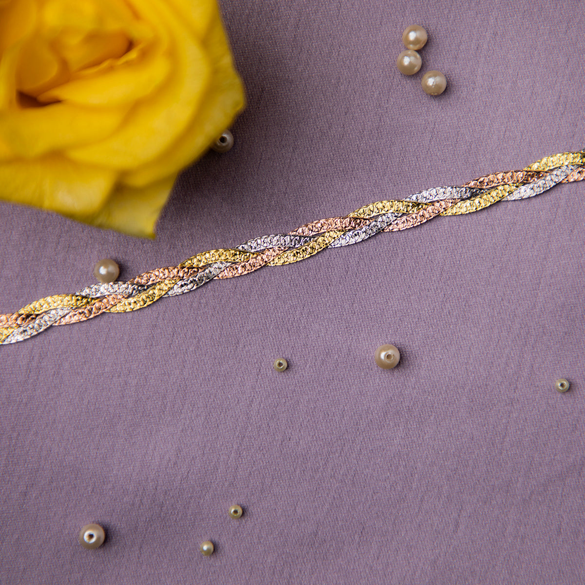 A close-up image of a sterling silver bracelet with a fishtail braid pattern, displayed on a textured background with a yellow flower and pearls scattered around.