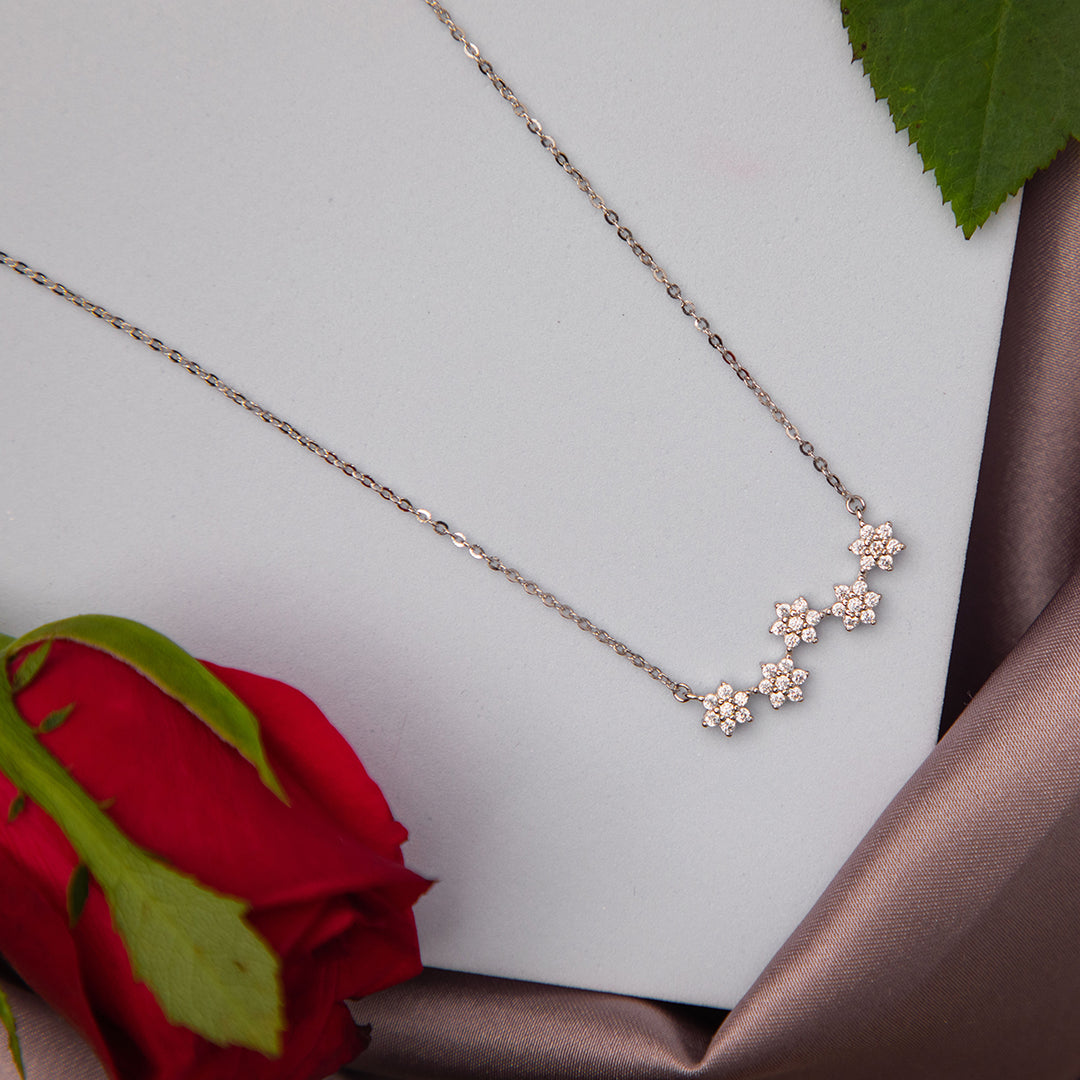 A silver pendant chain with five floral motifs, displayed on a white background with a red rose and green leaves in the foreground.