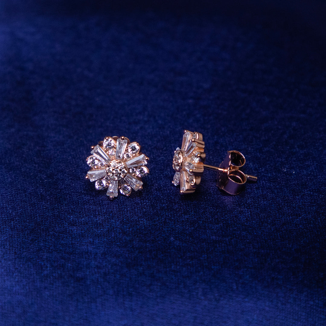 A pair of sterling silver earrings with a rose gold color finish, featuring floral embellishments on a blue background.
