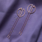 a pair of circle shaped rose gold color silver earrings dangler laid over a purple fabric with pearls sprinkled around it