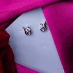 A pair of sterling silver stud earrings with white stones, displayed on a pink fabric.