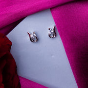 A pair of sterling silver stud earrings with white stones, displayed on a pink fabric.