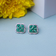 A pair of sterling silver stud earrings featuring a green floral motif, displayed on a textured background with a yellow flower for contrast.
