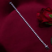 A heart-shaped cut tennis bracelet made of sterling silver, displayed on a red fabric surface with a red rose beside it.