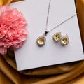 A sterling silver pendant set with a high shine finish and a pair of earrings, featuring a dazzling yellow stone pendant, displayed on a white surface with a pink flower and a gold-colored background.