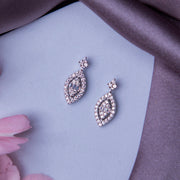 A pair of silver leaf motif embellished earrings displayed on a surface with a grey fabric and pink flowers around.