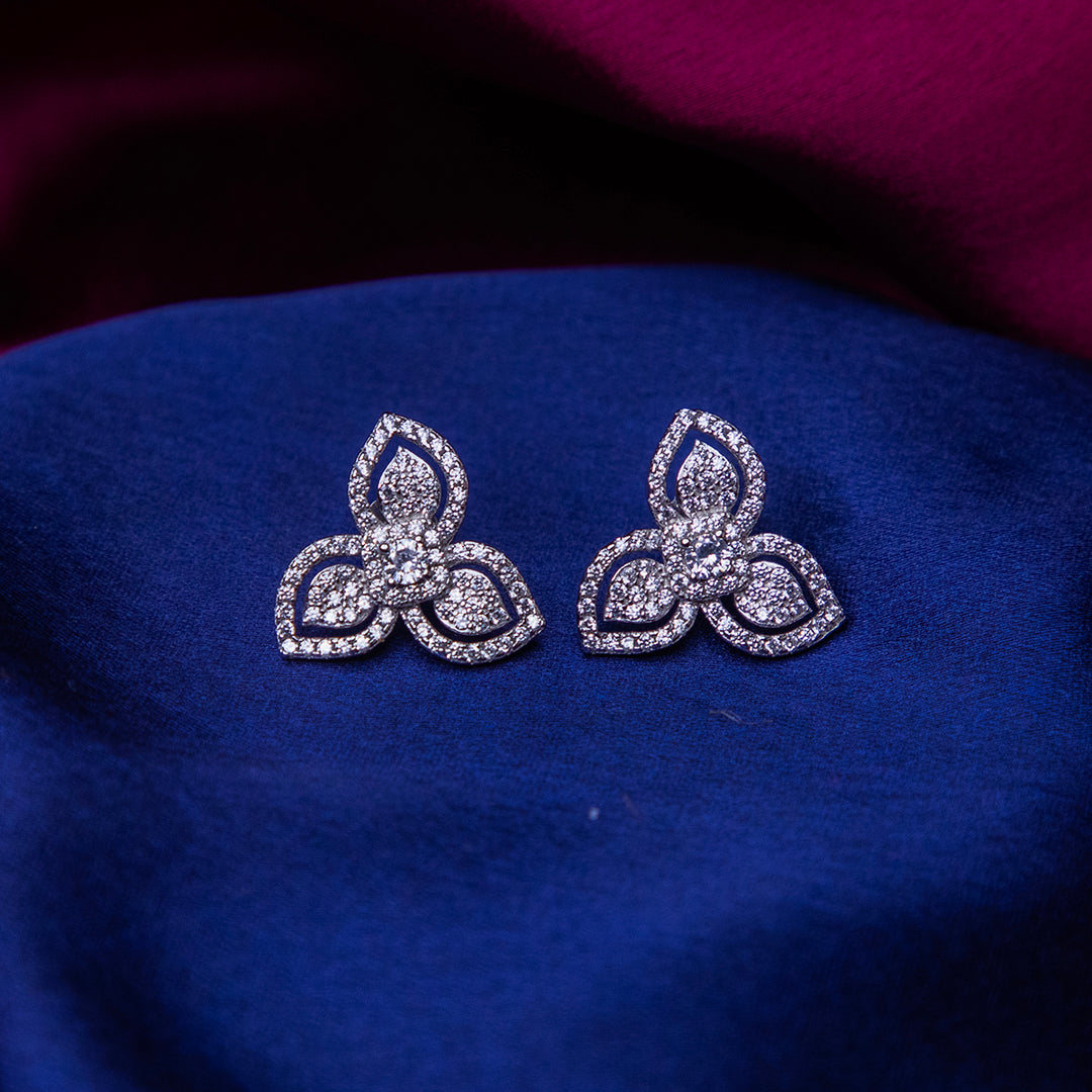 A pair of sterling silver stud earrings with an embellished leaflet design, displayed on a blue fabric.