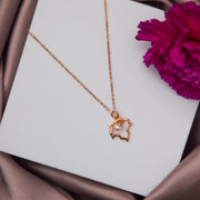 A rose gold-colored pendant chain with a maple leaf design and a central pearl, displayed on a white surface with a purple flower nearby.
