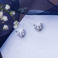 A pair of minimalistic white stone stud earrings placed on a white surface with a floral design in the background.