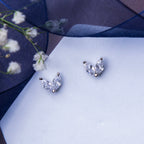 A pair of minimalistic white stone stud earrings placed on a white surface with a floral design in the background.