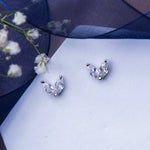 A pair of minimalistic white stone stud earrings placed on a white surface with a floral design in the background.