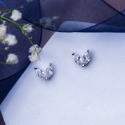 A pair of minimalistic white stone stud earrings placed on a white surface with a floral design in the background.