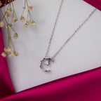 A silver pendant chain with a crescent moon design and a sparkling pear-cut white stone on a pink satin background with a flower in the background.