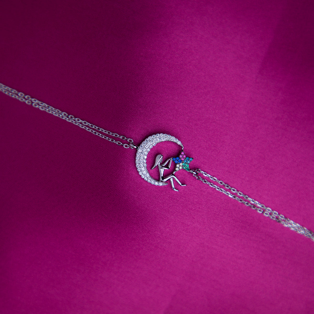A multicolor Selene charm bracelet with a silver rhodium-based coating, displayed on a pink background.