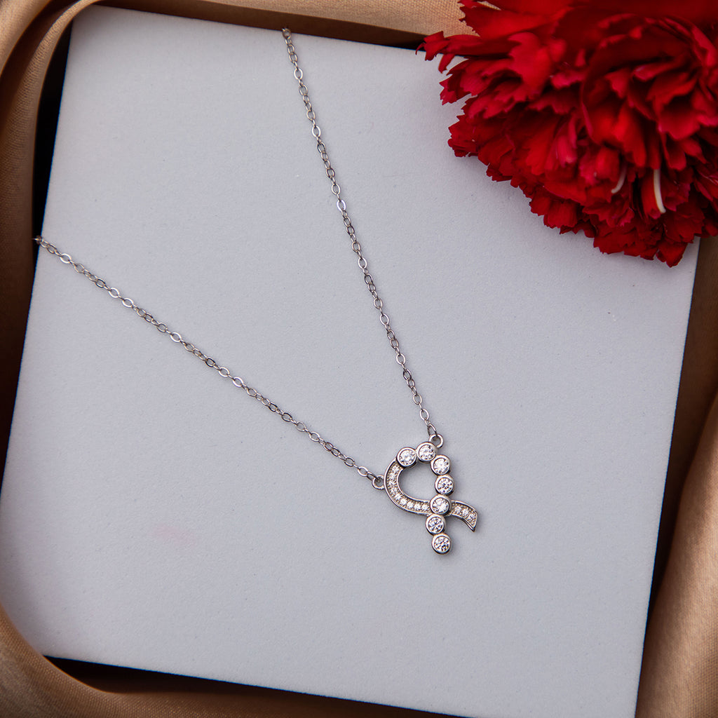 A silver pendant chain necklace with a heart-shaped pendant, presented on a white surface next to a red flower.