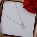 A silver pendant chain necklace with a heart-shaped pendant, presented on a white surface next to a red flower.