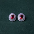 A pair of red gemstone stud earrings set in silver mounting, with a textured background.