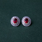 A pair of red gemstone stud earrings set in silver mounting, with a textured background.