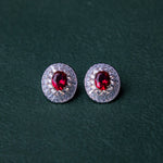 A pair of red gemstone stud earrings set in silver mounting, with a textured background.