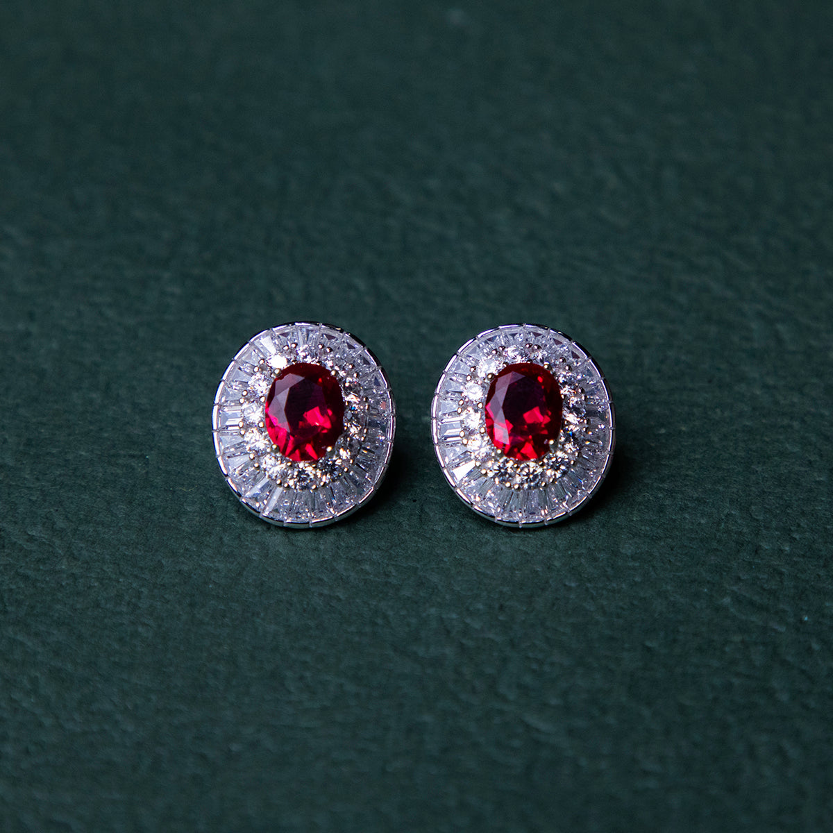 A pair of red gemstone stud earrings set in silver mounting, with a textured background.