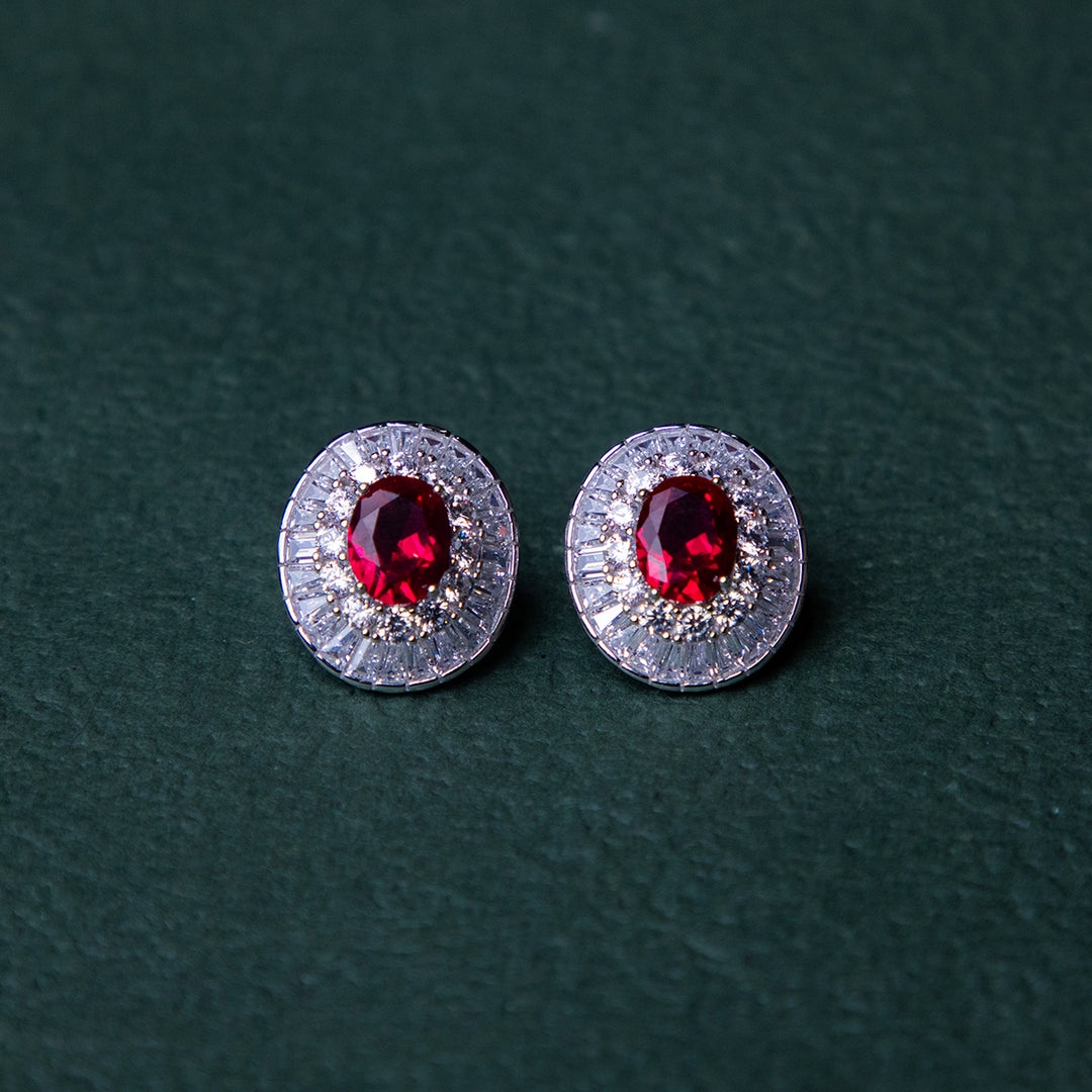 A pair of red gemstone stud earrings set in silver mounting, with a textured background.