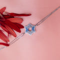 A sterling silver bracelet featuring a series of star-shaped charms with periwinkle blue gemstones, displayed on a pink background with a red flower scattered around.