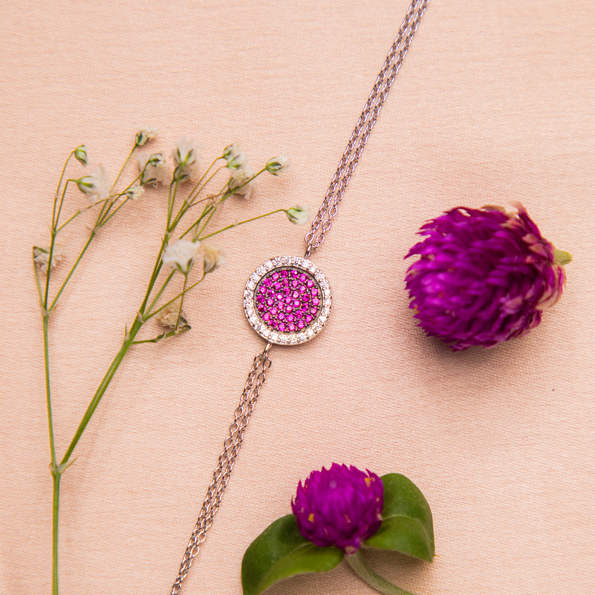 A sterling silver bracelet with a round pink gemstone charm, displayed on a neutral background with floral accents.