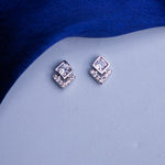 A pair of sterling silver stud earrings with a white stone setting on a blue textured background.