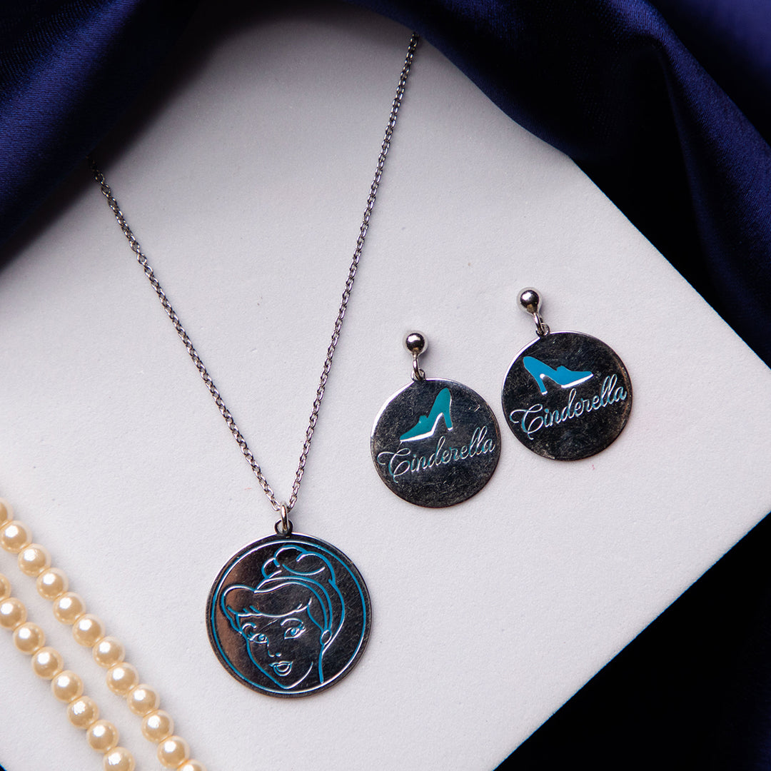A sterling silver pendant set featuring Cinderella's iconic glass slippers, with a blue and silver color scheme, displayed on a blue textured surface.