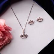 A sterling silver princess tiara pendant necklace accompanied by a pair of earrings, displayed on a white surface with a pink flower on the side.