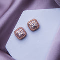 A pair of rose gold colored embellished stud earrings resting on a pale surface.