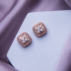 A pair of rose gold colored embellished stud earrings resting on a pale surface.