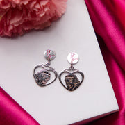 A pair of silver-colored earrings with a snow white impression design, displayed on a pink floral background.