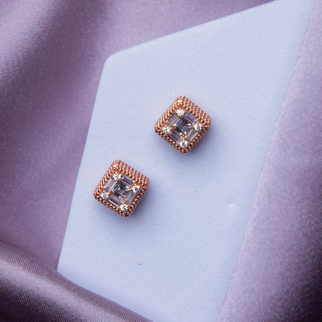 A pair of rose gold glittering silver stud earrings placed on a white surface with a blurred background.