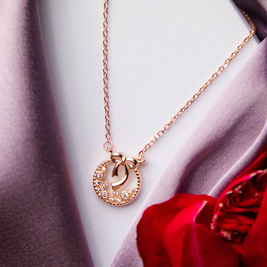 A rose gold wreath pendant chain in silver material, displayed on a mannequin wearing a grey coat and a red flower is visible in the foreground.