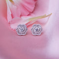 A pair of sterling silver rose-shaped stud earrings, displayed on a pink background with a petal motif.