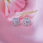 A pair of sterling silver rose-shaped stud earrings, displayed on a pink background with a petal motif.