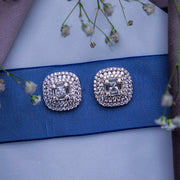 A pair of sterling silver statement stud earrings displayed on a blue fabric ribbon surface with small white flowers around them.