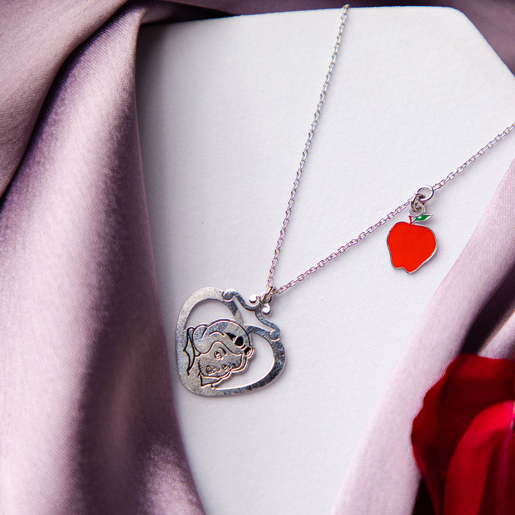 A silver-colored pendant chain necklace featuring a silhouette of Snow White within a heart-shaped frame, displayed on a white base with a purple scarf.