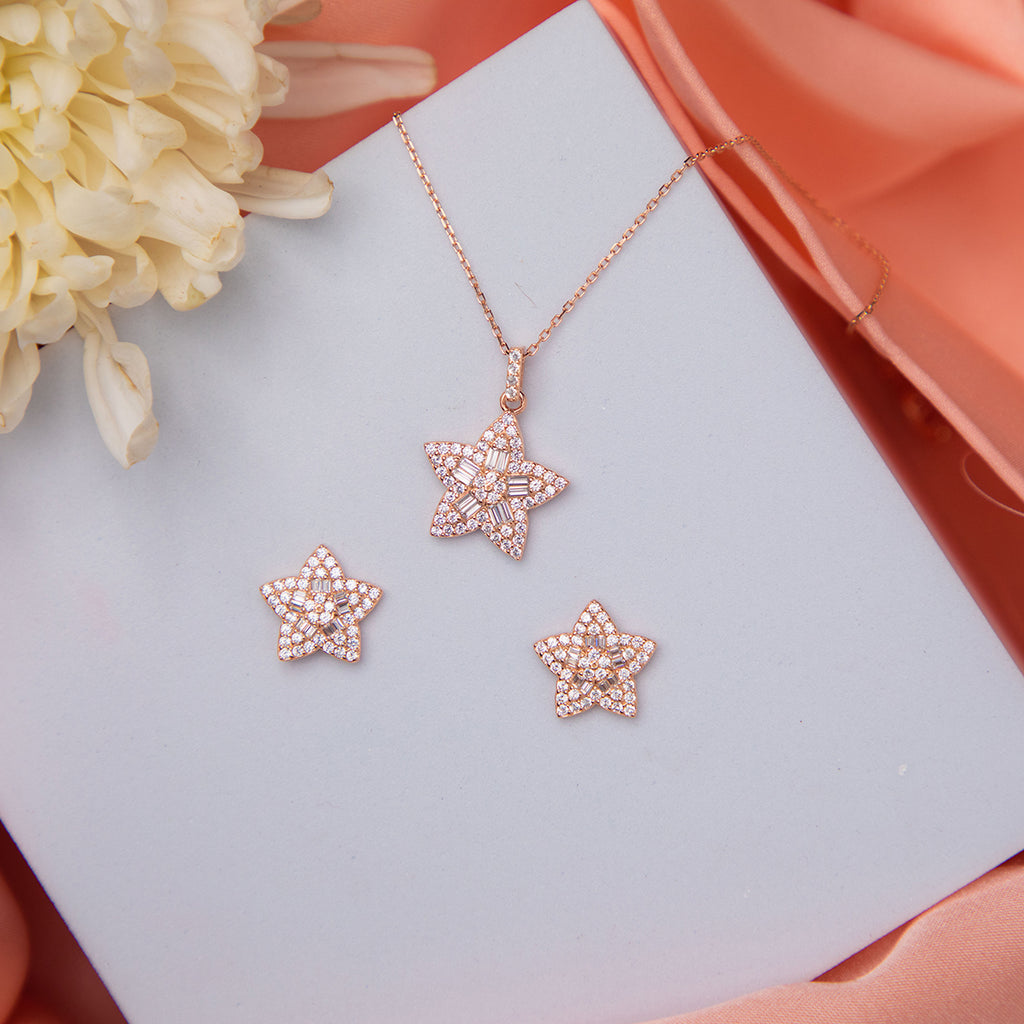 A sterling silver pendant set with a celestial motif and star-shaped embellishments, displayed on a rose gold-colored surface, accompanied by a pair of matching earrings.