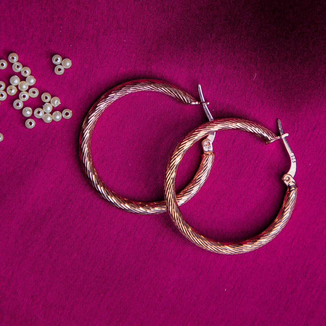 A pair of textured gold hoop earrings laid on a magenta pink surface along with pearls 