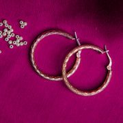 A pair of textured gold hoop earrings laid on a magenta pink surface along with pearls 