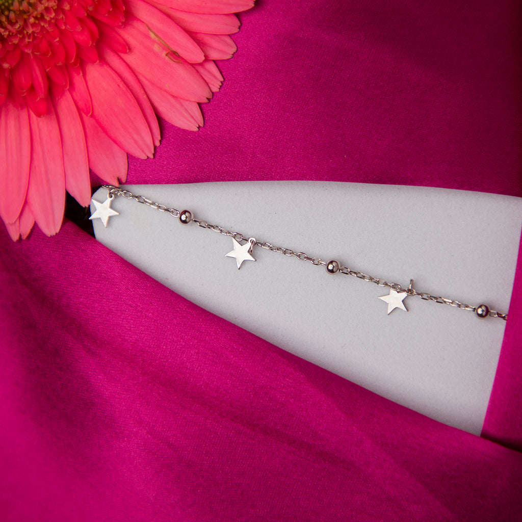 A sterling silver bracelet with star charms displayed on a pink fabric surface.