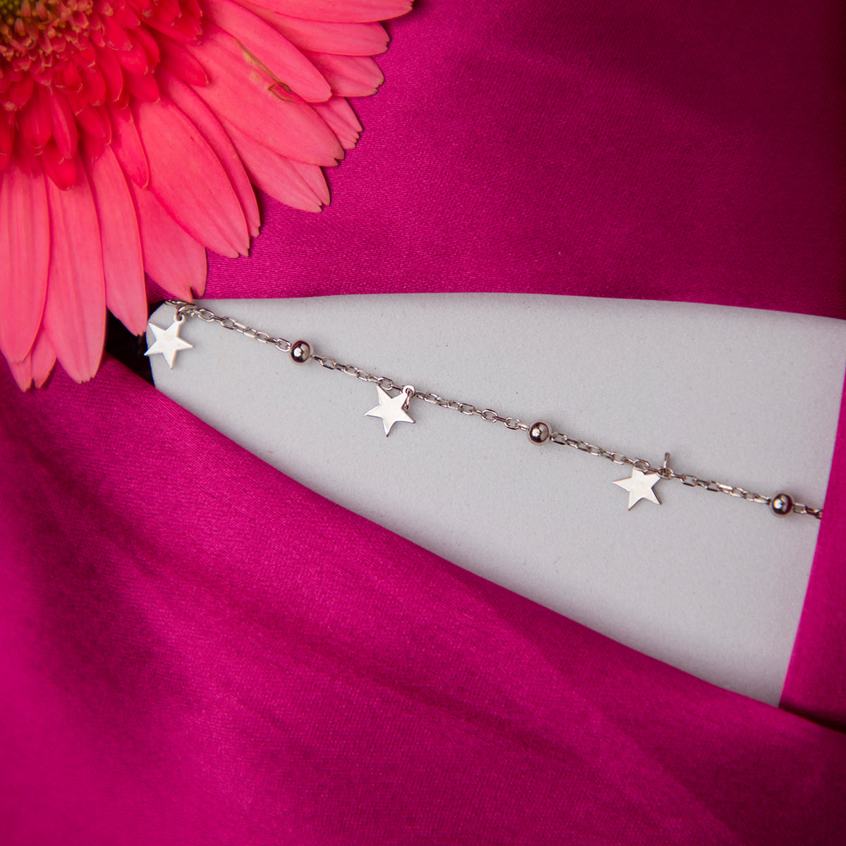 A sterling silver bracelet with star charms displayed on a pink fabric surface.