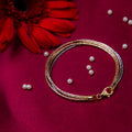 A sterling silver bracelet with a 5-layered design, featuring silver, rose gold and gold colors, displayed on a red background with a few pearls scattered around.